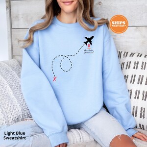 a woman sitting on a bed wearing a blue sweatshirt