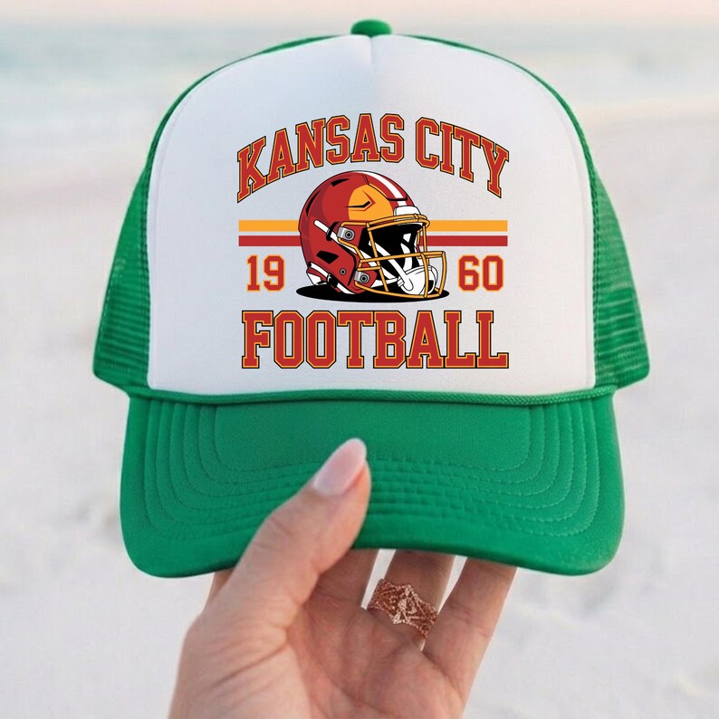 May include: A green and white trucker hat with the text "KANSAS CITY FOOTBALL" in red and gold. The hat features a football helmet graphic and the numbers "19 60".