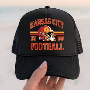 May include: Black trucker hat with the text "KANSAS CITY FOOTBALL" in red and gold, and a football helmet graphic. The hat also displays the numbers "19" and "60".