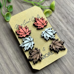May include: Set of six wooden maple leaf earrings in three different colors: red, white, and brown. The earrings are displayed on a brown card with the text "My Sweet Crafts & More".