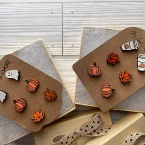 May include: Wooden fall-themed earrings in a gift box. Designs include pumpkins, maple leaves, ghosts, and coffee cups with pumpkins. The earrings are displayed on a brown card with the text "Mary Lou's Crafts & MORE".