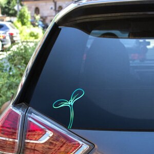 May include: A teal and blue sprout sticker is affixed to the rear window of a car. The sticker features a minimalist design of a young plant with two leaves and a stem, suggesting growth and nature.