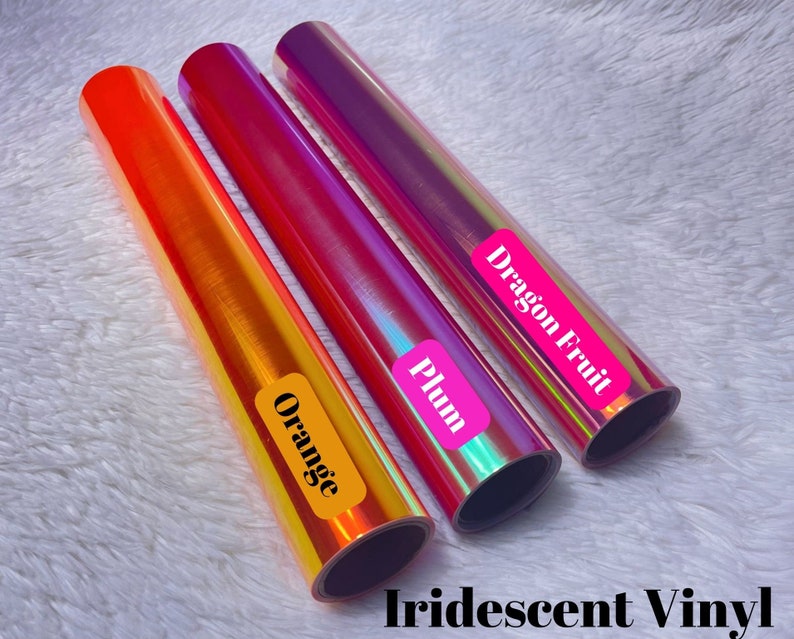 May include: Three rolls of iridescent vinyl in orange, plum, and dragon fruit colors. Each roll has a label with the color name. The text "Iridescent Vinyl" is at the bottom of the image.