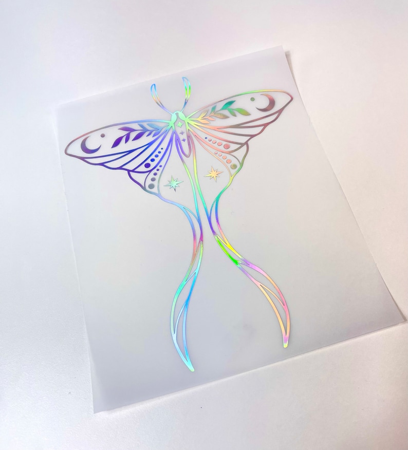 May include: A holographic iridescent sticker of a moth with intricate details, including leaves, moons, and stars. The moth is outlined in black and has a rainbow-like sheen.