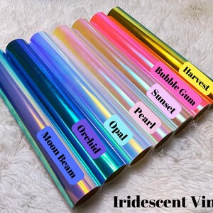 May include: Rolls of iridescent vinyl in various colors, including blue, purple, pink, and gold. Each roll is labeled with a color name, such as "Moon Beam" and "Harvest". The text "Iridescent Vinyl" is at the bottom.