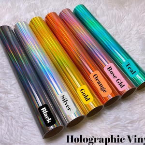 May include: Rolls of holographic vinyl in various colors, including black, silver, gold, orange, rose gold, and teal. Each roll is labeled with its color name. The text "Holographic Vinyl" is displayed at the bottom of the image.