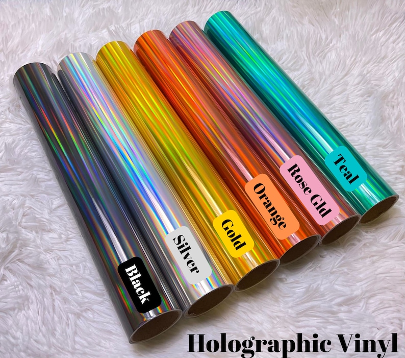 May include: Rolls of holographic vinyl in various colors, including black, silver, gold, orange, rose gold, and teal. Each roll is labeled with its color name. The text "Holographic Vinyl" is displayed at the bottom of the image.