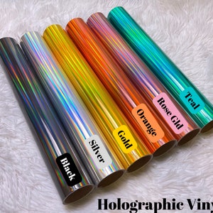 May include: Assortment of holographic vinyl rolls in black, silver, gold, orange, rose gold, and teal.  The rolls are labeled with their respective colors.  Holographic Vinyl.