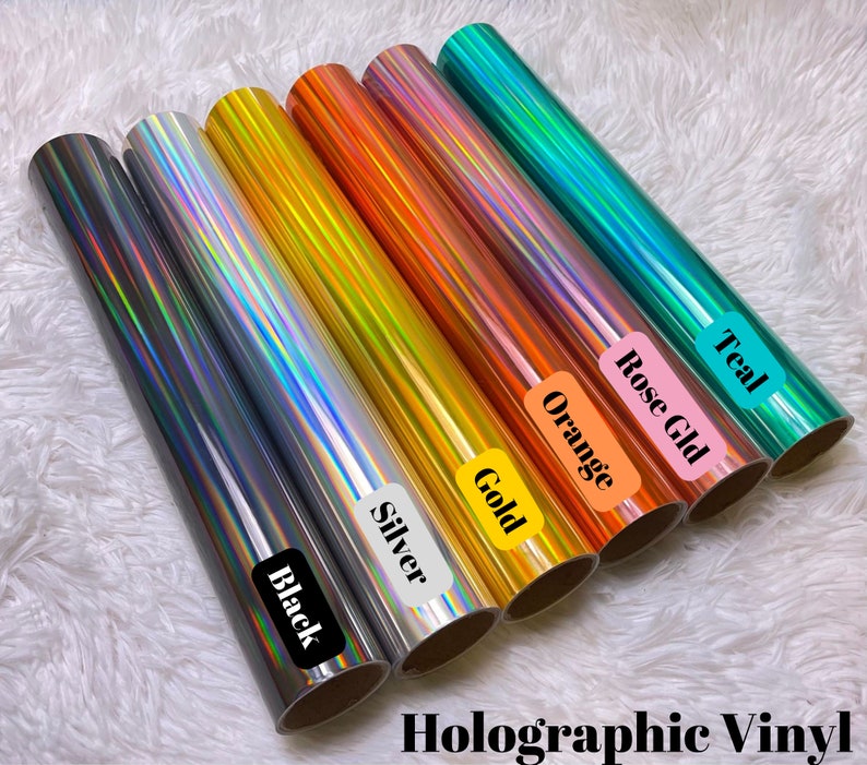 May include: Assortment of holographic vinyl rolls in black, silver, gold, orange, rose gold, and teal.  The rolls are labeled with their respective colors.  Holographic Vinyl.