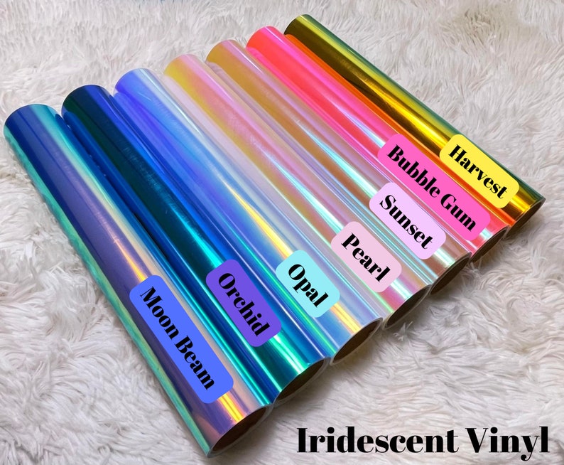 May include: A collection of iridescent vinyl rolls in various colors, including blue, green, pink, gold, and white. The rolls are labeled with names like "Moon Beam", "Orchid", "Opal", "Pearl", "Sunset", "Bubble Gum", and "Harvest".