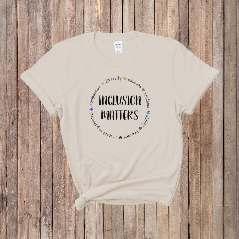 May include: A beige t-shirt with a circle graphic that says "Inclusion Matters" surrounded by words like "diversity", "educate", "compassion", "potential", "respect", "bravery", "ability", "kindness", and "unity".