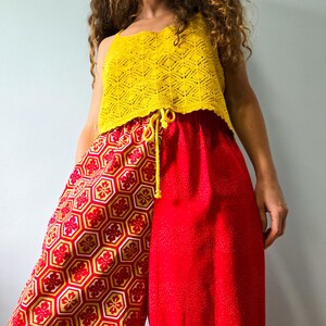 May include: A bright yellow sleeveless crochet top with a textured diamond pattern paired with wide-leg trousers. The trousers feature a split design with one side in a red and yellow geometric floral hexagon print and the other in solid red.