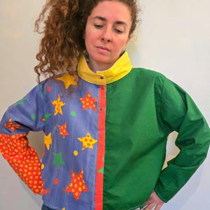 May include: A colorful jacket with a split design. One side is green, the other is blue with yellow and red stars. The collar is yellow, and the sleeves are red with yellow polka dots. The jacket has a button-up front.