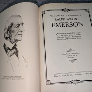 May include: Open book with a portrait of Ralph Waldo Emerson and the title "The Complete Writings of Ralph Waldo Emerson." The book is Volume 1, published by WM. H. Wise & Co. in New York. The book's pages are off-white.