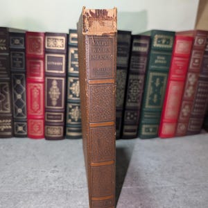 May include: A vintage brown book with the title "Ralph Waldo Emerson Complete Writings" visible on the spine. The book has a textured cover and is part of a collection of antique books.
