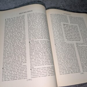 May include: An open book with aged, yellowed pages. The text, titled "SELF-RELIANCE," is printed in black ink. The book is slightly open, revealing the text and the aged paper texture. The book is likely an antique or vintage edition.