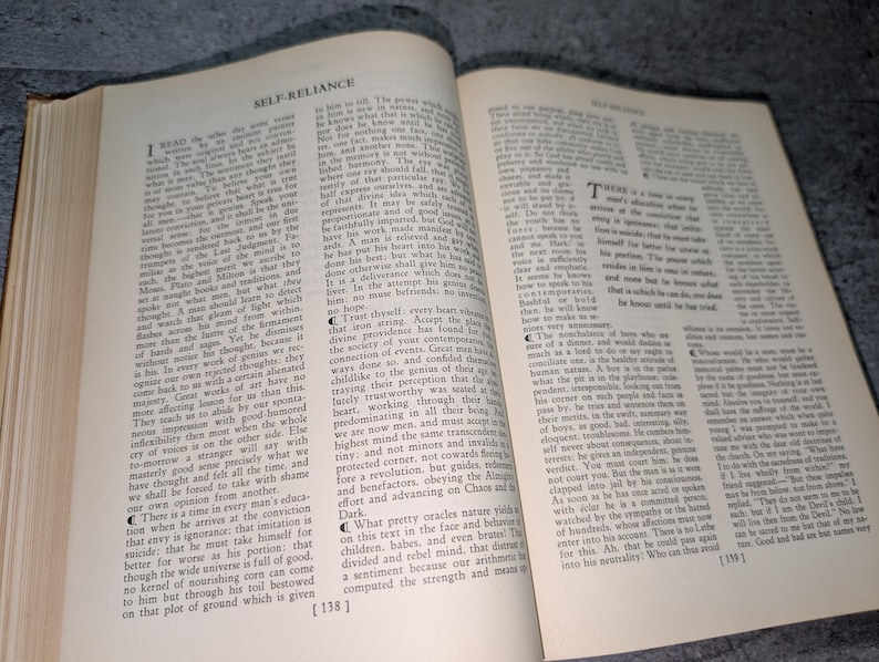 May include: An open book with aged, yellowed pages. The text, titled "SELF-RELIANCE," is printed in black ink. The book is slightly open, revealing the text and the aged paper texture. The book is likely an antique or vintage edition.