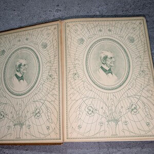 May include: Open book with two facing pages. Each page features a portrait of a man in an oval frame, surrounded by a decorative floral and geometric design in green on a cream background. The book's edges are brown.