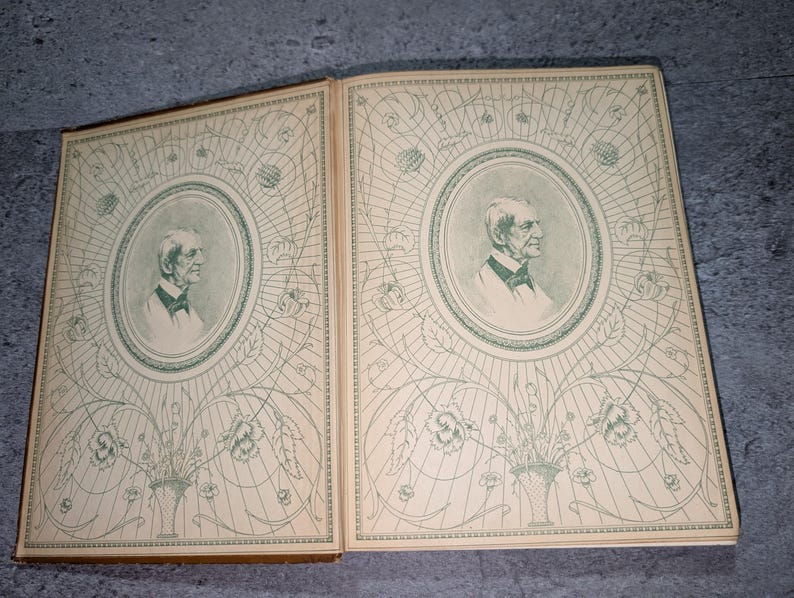 May include: Open book with two facing pages. Each page features a portrait of a man in an oval frame, surrounded by a decorative floral and geometric design in green on a cream background. The book's edges are brown.