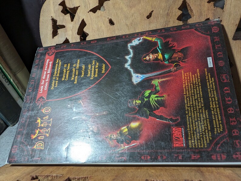 Op de afbeelding: De achterkant van een Diablo II videogamedoos. De doos is rood en zwart met een zilveren schild in het midden. Het schild heeft het Diablo II-logo erop. De achterkant van de doos vermeldt andere games van Blizzard Entertainment, waaronder Warcraft III, StarCraft en Brood War.