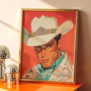 May include: Framed art print featuring a portrait of a man in a white cowboy hat with jewel embellishments. The artwork has a red background and a gold frame. The man is wearing a turquoise shirt and a patterned jacket.