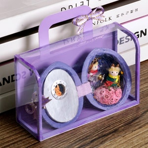 May include: A purple, clear plastic box with a handle, containing two miniature, hand-crafted, egg-shaped,  dioramas. One diorama features a miniature prince and princess, the other features a miniature fox.