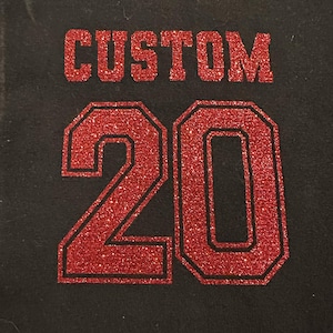 May include: Black fabric with the word "CUSTOM" in red glitter lettering above the number "20". The number "20" is also in red glitter with a black outline.