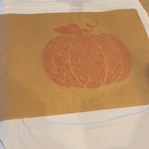 May include: A brown paper stencil with a red pumpkin design. The pumpkin has a swirling pattern.