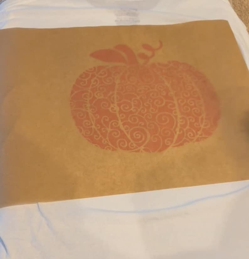 May include: A brown paper stencil with a red pumpkin design. The pumpkin has a swirling pattern.