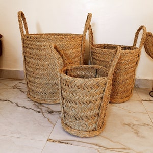 Könnte beinhalten: Drei geflochtene Körbe in verschiedenen Größen mit Griffen. Die Körbe sind aus natürlichen Materialien gefertigt und haben eine hellbraune Farbe.