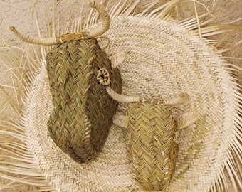 May include: Two woven straw animal heads, one larger than the other, are displayed on a woven straw mat with a fringe border. The animal heads are brown and have a woven texture.