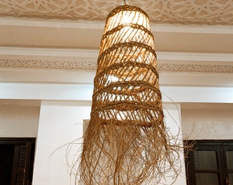 May include: A woven wicker pendant light with a fringe of natural fibers hangs from a ceiling with a decorative, white, patterned design.