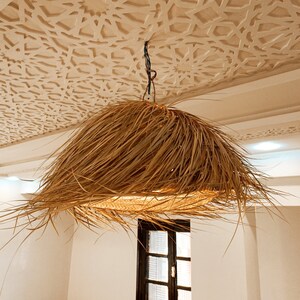 May include: A large, round, woven light fixture hangs from a ceiling with a decorative, white, geometric pattern. The fixture is made of natural materials and has a light brown color.