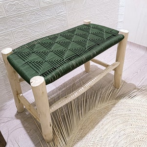 Op de afbeelding: Een groene geweven bank met een naturel houten frame. De bank staat op een geweven kleed.