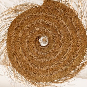 Może przedstawiać: Duża, okrągła, pleciona lampa wykonana z naturalnych materiał&oacute;w. Lampa ma spiralny wz&oacute;r i żar&oacute;wkę w środku.