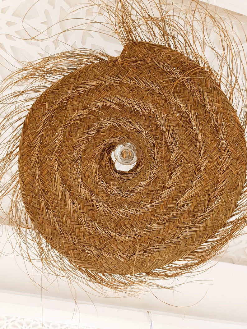 Może przedstawiać: Duża, okrągła, pleciona lampa wykonana z naturalnych materiał&oacute;w. Lampa ma spiralny wz&oacute;r i żar&oacute;wkę w środku.
