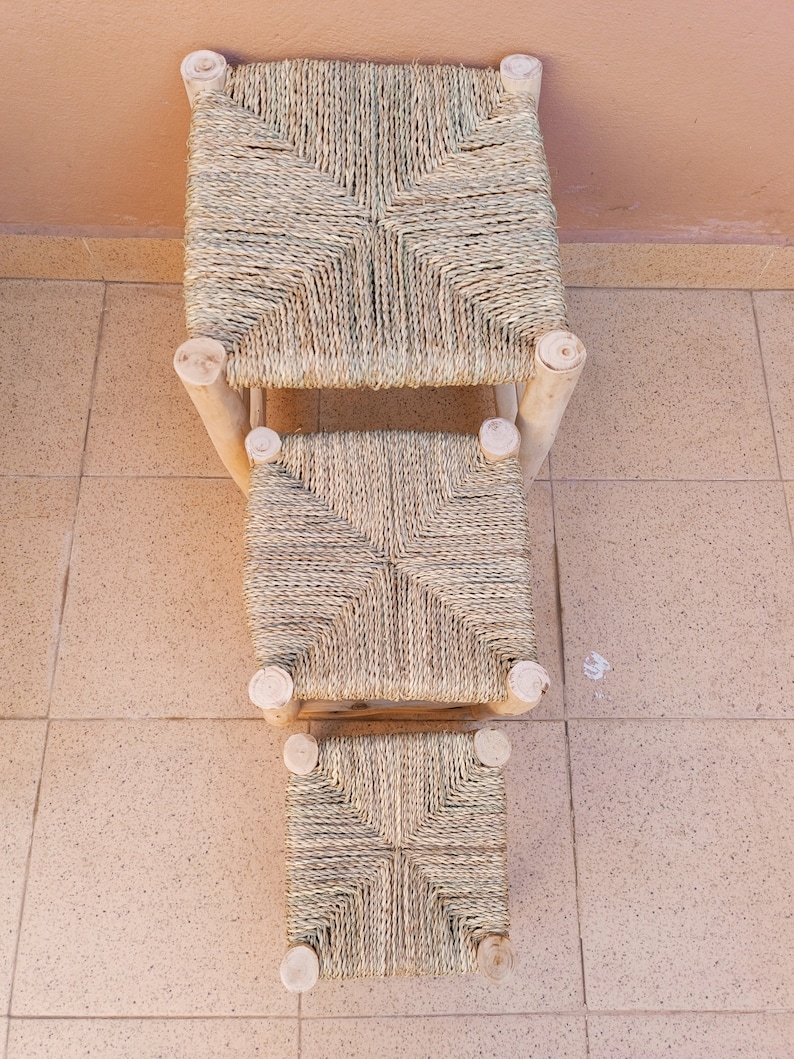 May include: Three woven straw ottomans with wooden frames. The ottomans are stacked on top of each other, with the largest ottoman on the bottom and the smallest ottoman on top.