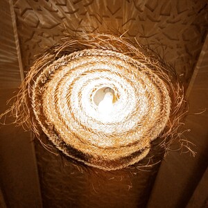 May include: A woven straw lampshade with a light bulb inside, hanging from a ceiling.