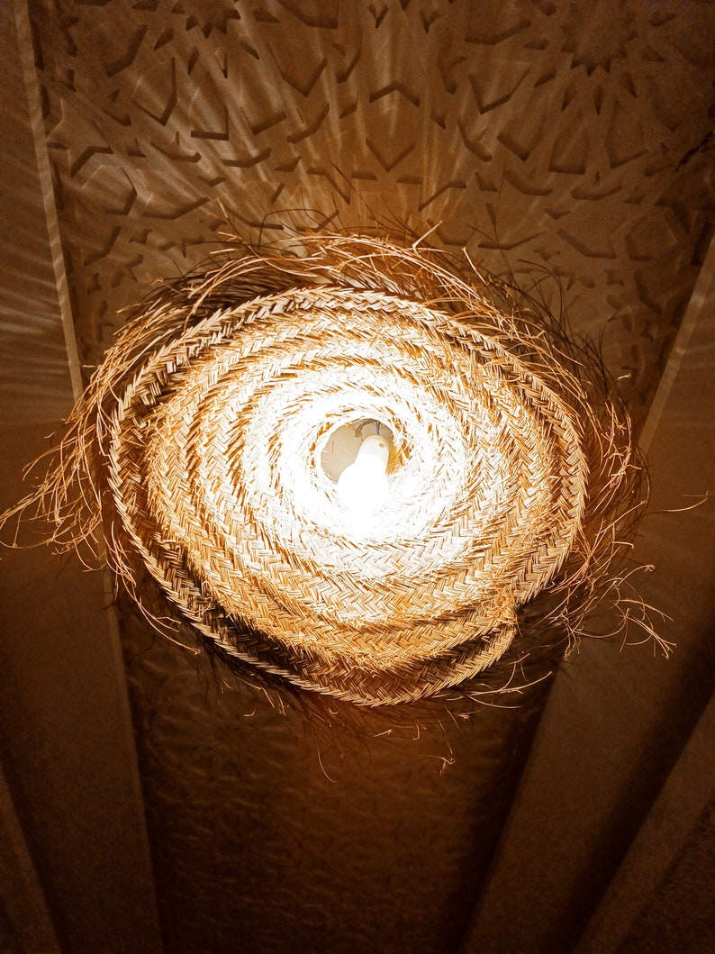 May include: A woven straw lampshade with a light bulb inside, hanging from a ceiling.