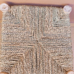 May include: A woven chair seat with a natural straw colour and a criss-cross pattern. The seat is made of natural materials and has a rustic look.