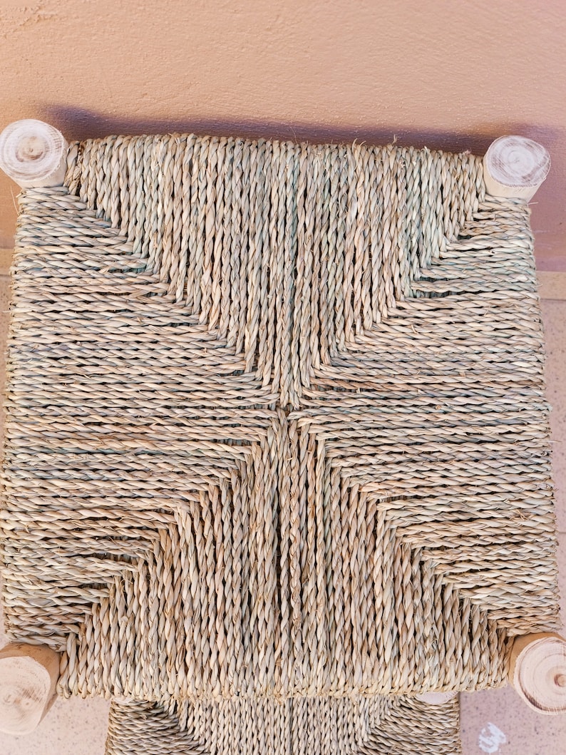 May include: A woven chair seat with a natural straw colour and a criss-cross pattern. The seat is made of natural materials and has a rustic look.