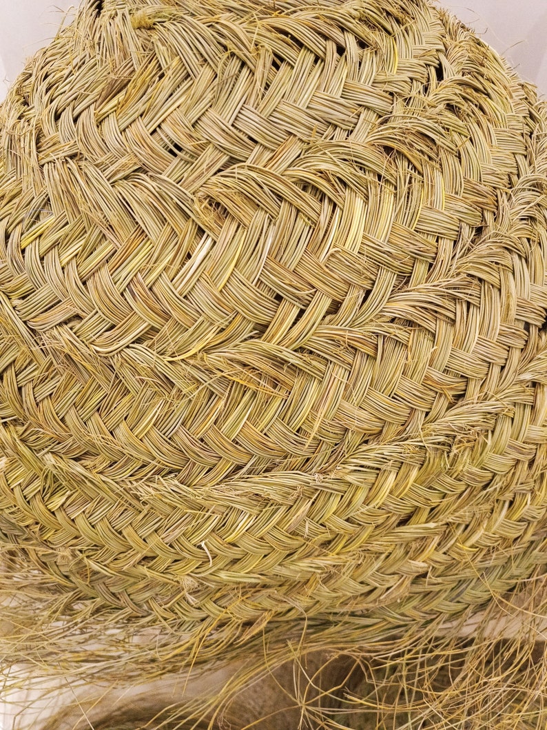 K&ouml;nnte beinhalten: Nahaufnahme eines geflochtenen Korbes aus nat&uuml;rlichem, hellgelbem Stroh. Der Korb hat eine runde Form mit einem dicht gewebten Muster, das die komplizierte Handwerkskunst zeigt. Die Textur ist rau und organisch, mit einigen losen Str&auml;hnen.