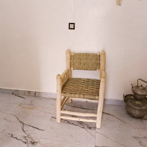 Pode incluir: Uma cadeira de madeira com assento e encosto de vime. A cadeira &eacute; de cor castanho claro e tem um design simples. A cadeira est&aacute; sentada num ch&atilde;o de ladrilhos brancos.