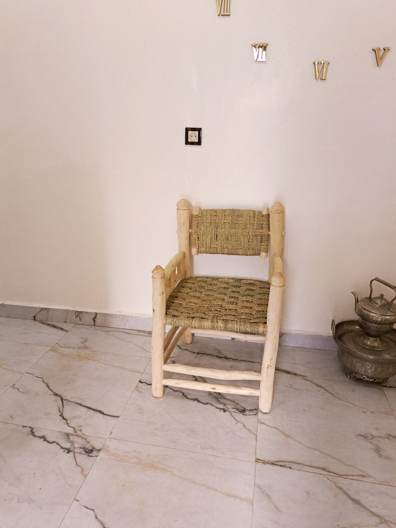 Pode incluir: Uma cadeira de madeira com assento e encosto de vime. A cadeira &eacute; de cor castanho claro e tem um design simples. A cadeira est&aacute; sentada num ch&atilde;o de ladrilhos brancos.