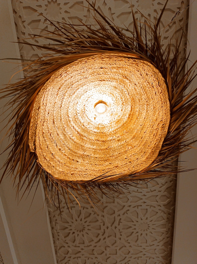 May include: A woven, round, straw lampshade with a light bulb inside. The lampshade is surrounded by dried palm fronds.
