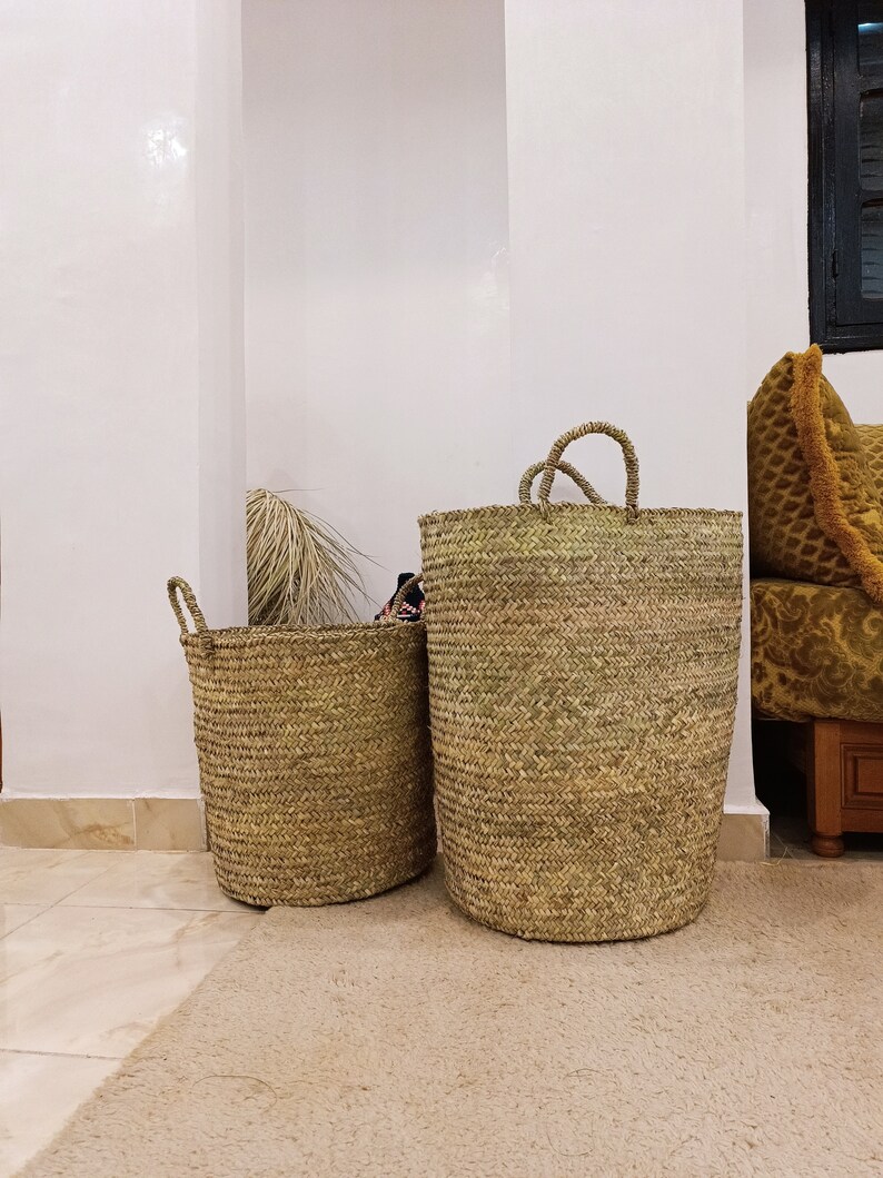 May include: Two woven seagrass baskets with handles. The larger basket is taller and wider than the smaller basket. Both baskets are a natural beige color.