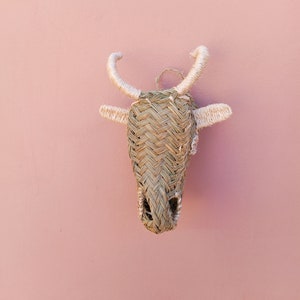 May include: A woven straw bull's head wall decor with white accents. The bull's head is a traditional craft item and is a popular choice for home decor.