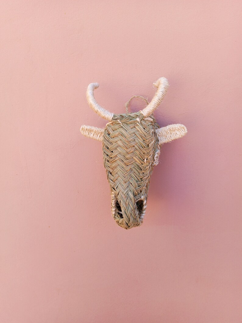 May include: A woven straw bull's head wall decor with white accents. The bull's head is a traditional craft item and is a popular choice for home decor.