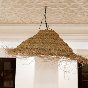May include: A woven, straw lampshade hangs from a white ceiling with a decorative, geometric pattern. The lampshade is brown and has a natural, rustic look.