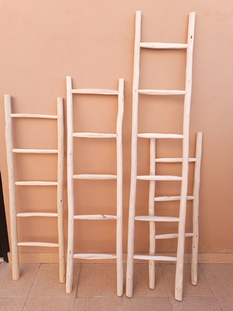 Puede incluir: Cinco escaleras de madera blanca de diferentes alturas apoyadas en una pared de color melocot&oacute;n. Las escaleras tienen de cuatro a seis pelda&ntilde;os cada una.